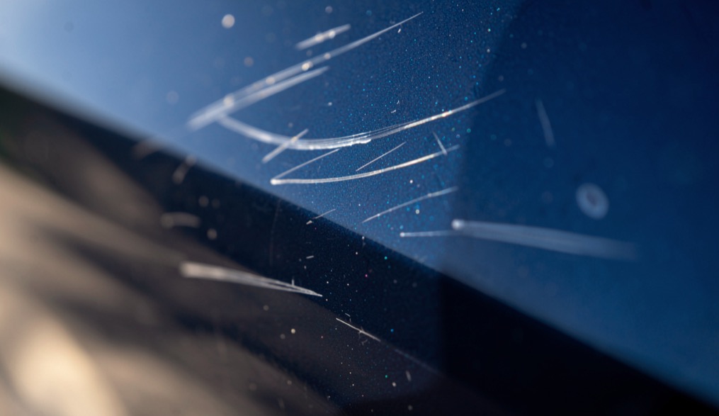 Gros plan sur la portière d'une voiture bleu foncé avec quelques fines rayures claires parallèles dans le vernis, vues en lumière rasante
